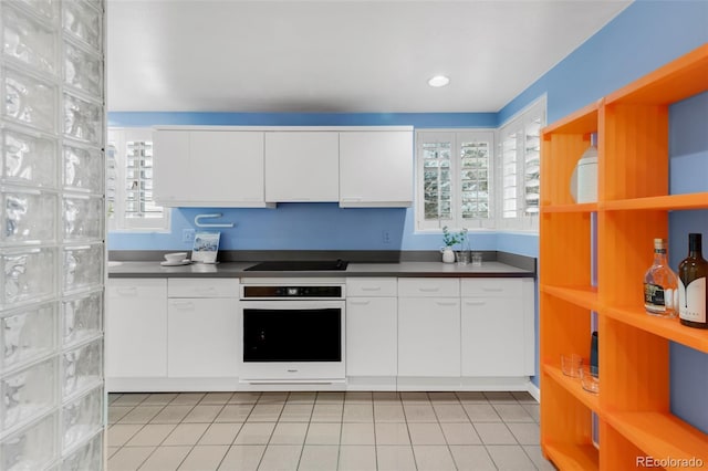 kitchen featuring light tile patterned floors, dark countertops, white cabinetry, white oven, and black electric stovetop