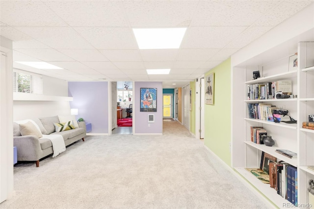 living area featuring a drop ceiling, baseboards, and carpet flooring