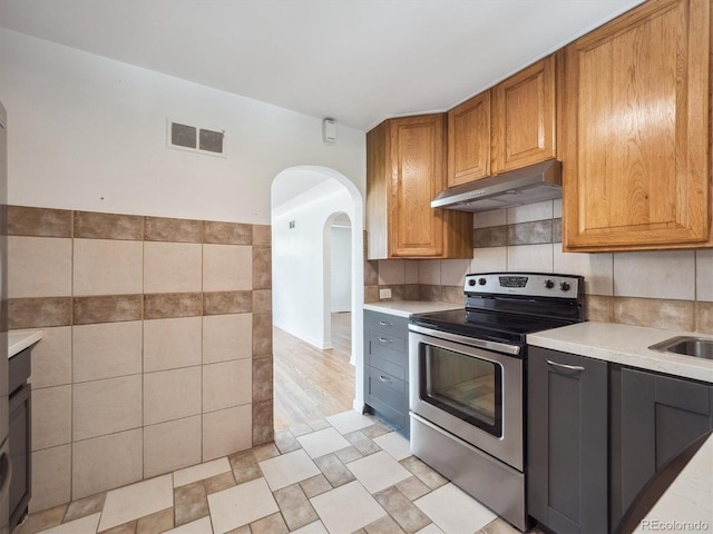 3050 S Delaware St, Englewood, CO 80110 - kitchen featuring stainless steel range with electric stovetop, under cabinet range hood, light countertops, arched walkways, and brown cabinetry
