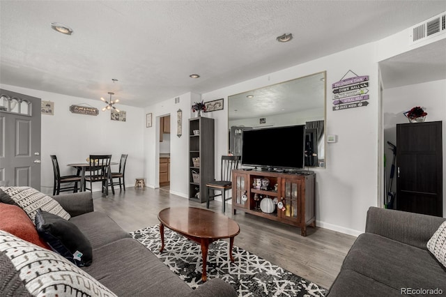 living area featuring visible vents, a textured ceiling, wood finished floors, an inviting chandelier, and baseboards