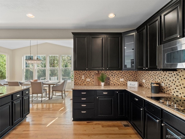 41 Garner Ln, Erie, CO 80516 - kitchen featuring dark cabinets, stainless steel microwave, tasteful backsplash, light wood-style floors, and glass insert cabinets