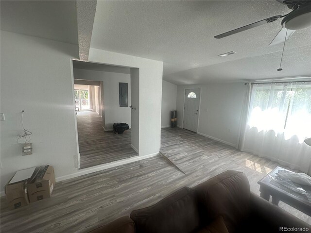 interior space with a ceiling fan, electric panel, a textured ceiling, wood finished floors, and baseboards