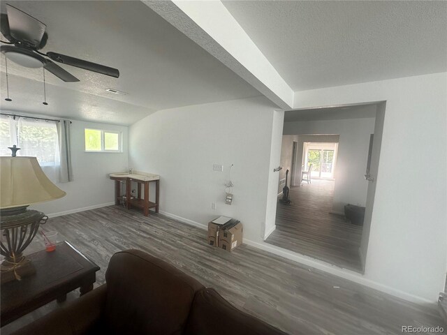 living area featuring a textured ceiling, wood finished floors, baseboards, ceiling fan, and vaulted ceiling