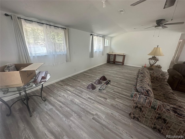 living room featuring visible vents, wood finished floors, baseboards, ceiling fan, and vaulted ceiling