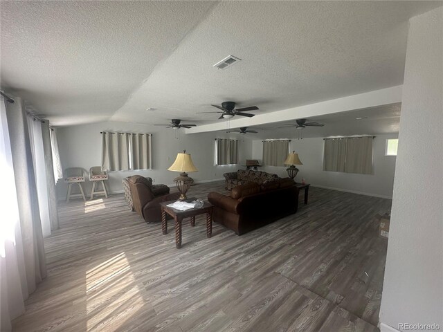 living area featuring lofted ceiling, wood finished floors, visible vents, and a textured ceiling