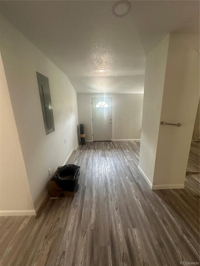 unfurnished living room featuring electric panel, a textured ceiling, baseboards, and wood finished floors