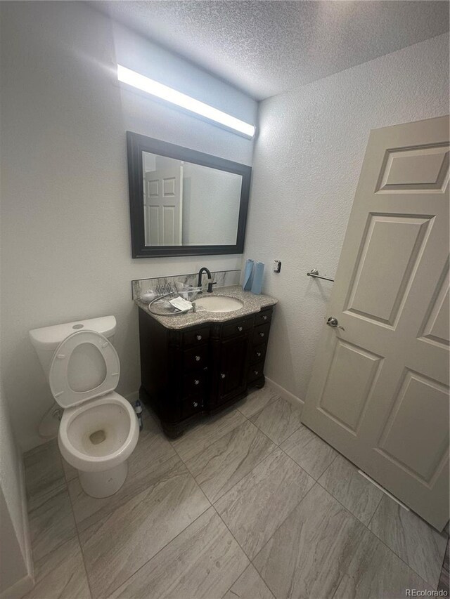 bathroom featuring vanity, toilet, marble finish floor, and a textured ceiling