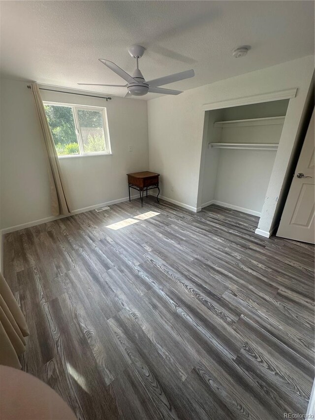 unfurnished bedroom featuring a textured ceiling, a closet, baseboards, ceiling fan, and dark wood-style flooring