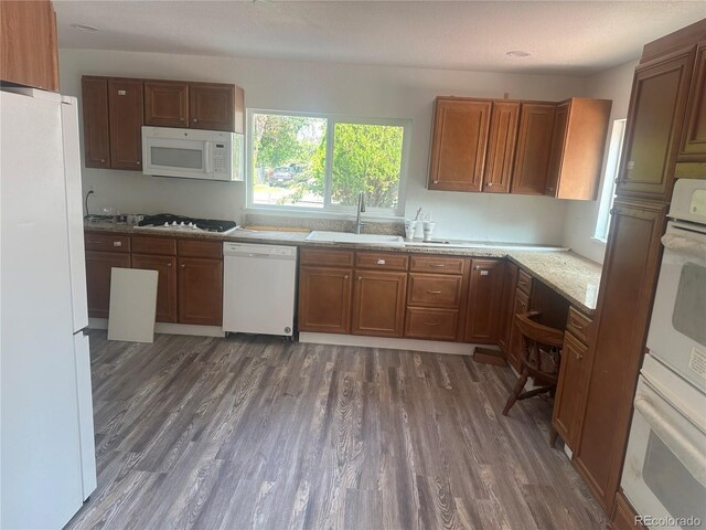 kitchen featuring brown cabinetry, white appliances, dark wood-type flooring, and a sink