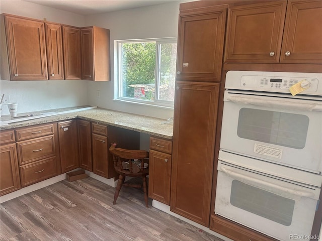 kitchen with light wood-type flooring, white double oven, brown cabinetry, and built in study area