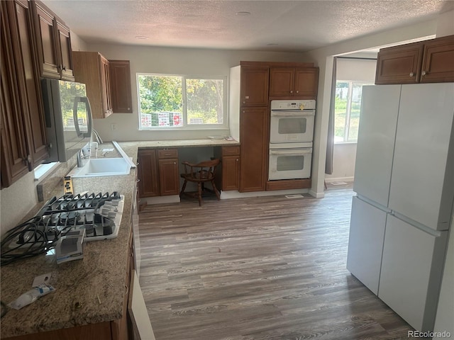 kitchen featuring a sink, white appliances, a textured ceiling, and wood finished floors