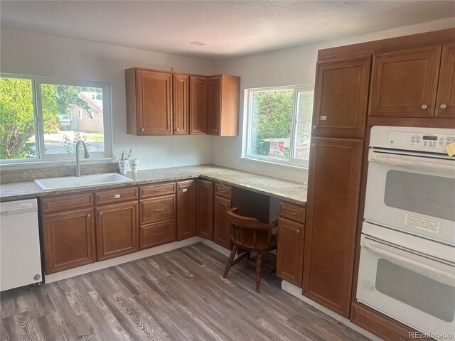 kitchen featuring a sink, wood finished floors, built in desk, white appliances, and light stone countertops