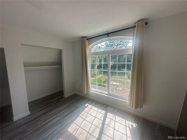 unfurnished bedroom with wood finished floors, visible vents, a closet, and baseboards