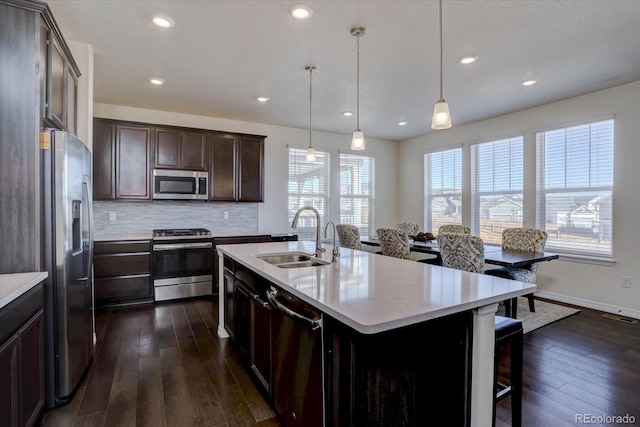 kitchen with pendant lighting, sink, stainless steel appliances, tasteful backsplash, and an island with sink