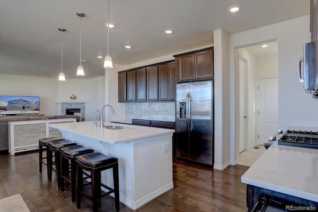 kitchen with sink, dark brown cabinets, stainless steel appliances, a center island with sink, and decorative light fixtures