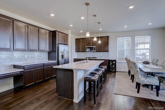 kitchen with dark hardwood / wood-style floors, an island with sink, a kitchen bar, hanging light fixtures, and stainless steel appliances