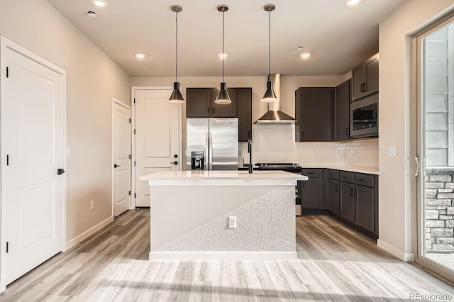 kitchen with stainless steel fridge, built in microwave, wall chimney range hood, range, and an island with sink