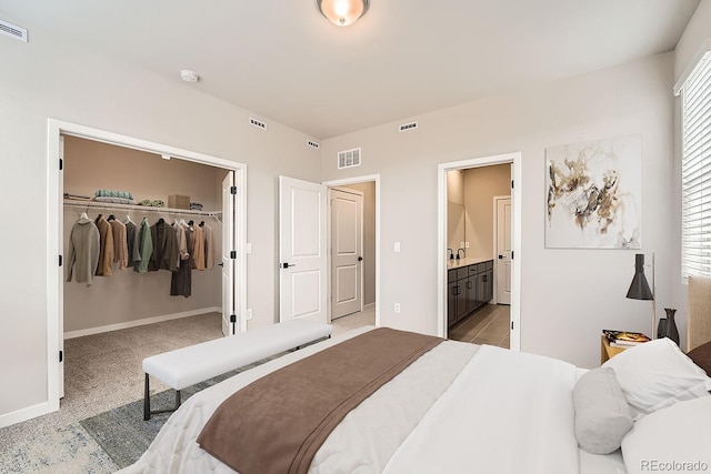 carpeted bedroom with ensuite bath, a walk in closet, sink, and a closet