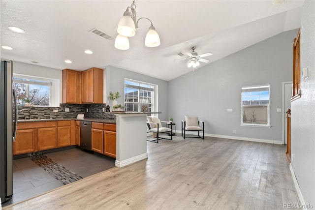 kitchen featuring lofted ceiling, kitchen peninsula, pendant lighting, stainless steel appliances, and decorative backsplash