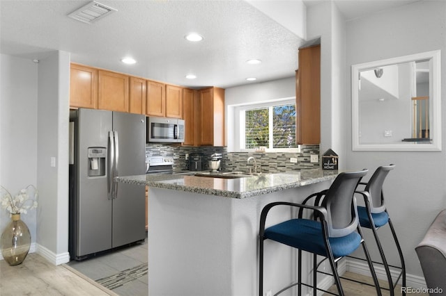 kitchen with stone counters, appliances with stainless steel finishes, backsplash, a kitchen bar, and kitchen peninsula