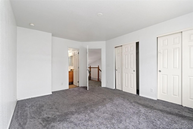 unfurnished bedroom featuring multiple closets, ensuite bathroom, and dark colored carpet