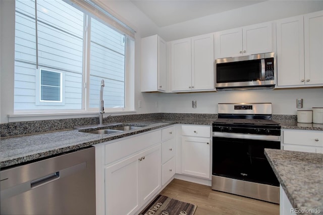 kitchen with appliances with stainless steel finishes, white cabinetry, dark stone countertops, and sink