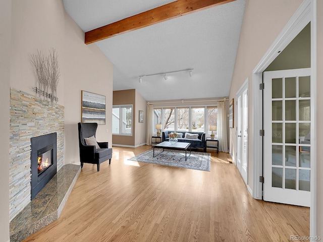 living area featuring beam ceiling, a stone fireplace, track lighting, wood finished floors, and high vaulted ceiling