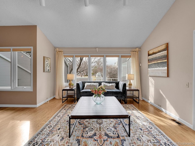 living room featuring light wood-type flooring, lofted ceiling, visible vents, and baseboards