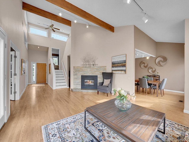 living room featuring a stone fireplace, wood finished floors, a towering ceiling, baseboards, and beamed ceiling