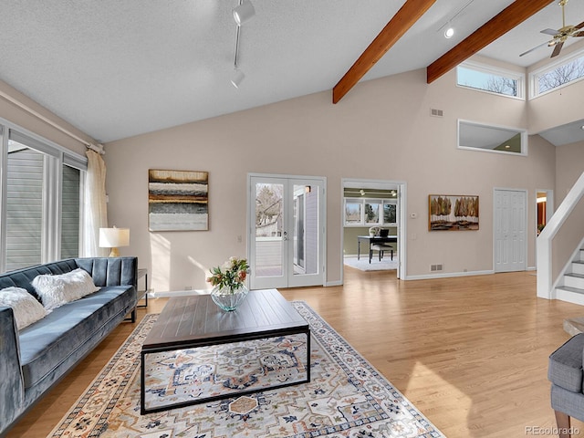 living room with ceiling fan, lofted ceiling with beams, visible vents, light wood-style floors, and stairway