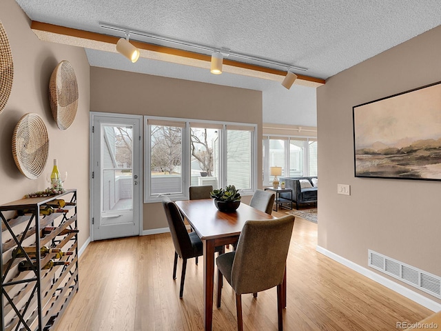 dining area featuring a textured ceiling, light wood finished floors, visible vents, and baseboards