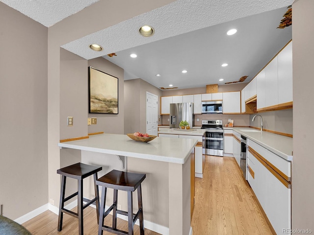 kitchen with stainless steel appliances, light wood-type flooring, light countertops, and white cabinets