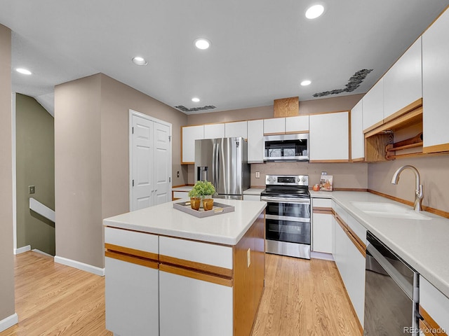 kitchen with stainless steel appliances, a sink, white cabinetry, light wood-style floors, and a center island