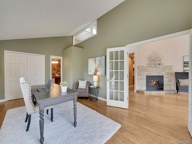 office featuring light wood-style flooring, high vaulted ceiling, a stone fireplace, and baseboards