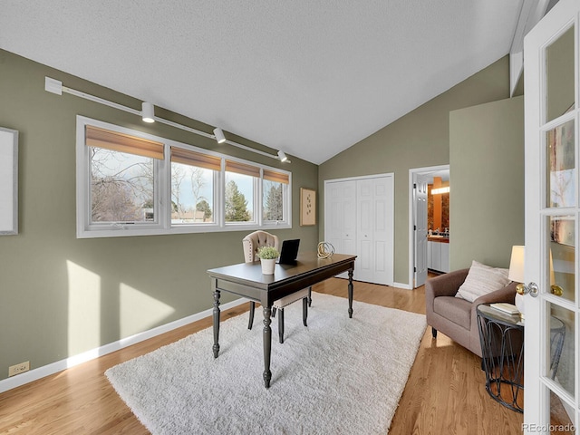 office area with light wood-style floors, vaulted ceiling, and baseboards