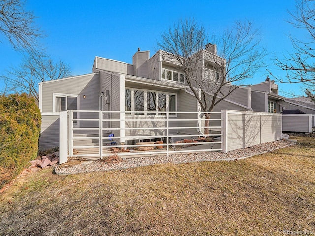 back of house featuring a lawn, a chimney, and fence