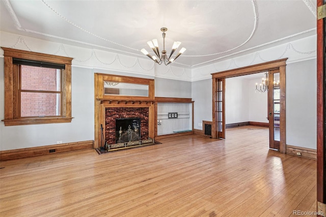 unfurnished living room with baseboards, hardwood / wood-style floors, an inviting chandelier, french doors, and a brick fireplace