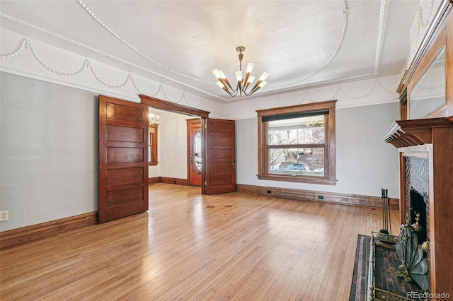 unfurnished living room featuring light wood-style floors, a fireplace, a notable chandelier, and baseboards