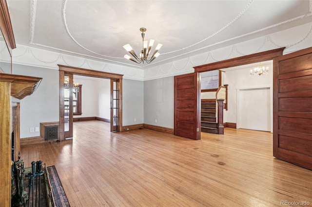 unfurnished living room with a chandelier, light wood-type flooring, french doors, and stairs