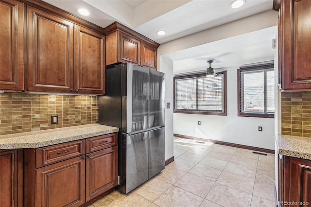 kitchen with tasteful backsplash, visible vents, baseboards, light stone counters, and freestanding refrigerator