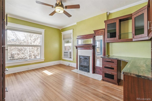 unfurnished living room with crown molding, light wood-style floors, a fireplace with flush hearth, ceiling fan, and baseboards