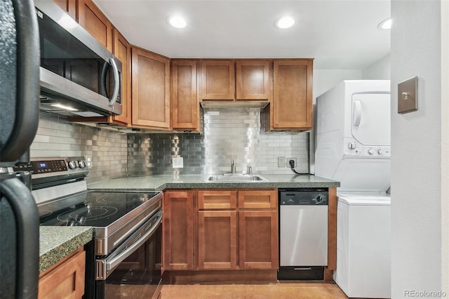 kitchen featuring stacked washing maching and dryer, stainless steel appliances, a sink, and brown cabinetry