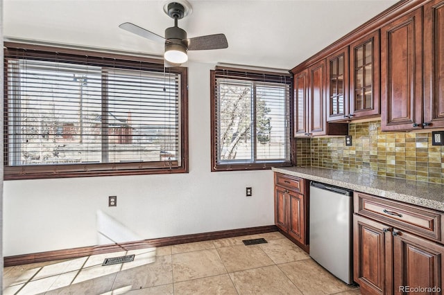 kitchen featuring light stone counters, refrigerator, visible vents, decorative backsplash, and glass insert cabinets