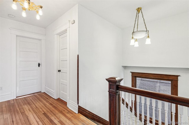 corridor featuring an inviting chandelier, baseboards, light wood finished floors, and an upstairs landing