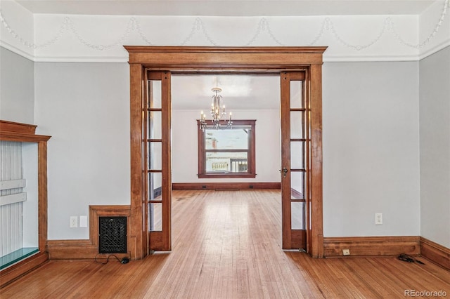 unfurnished dining area featuring french doors, baseboards, a chandelier, and hardwood / wood-style floors