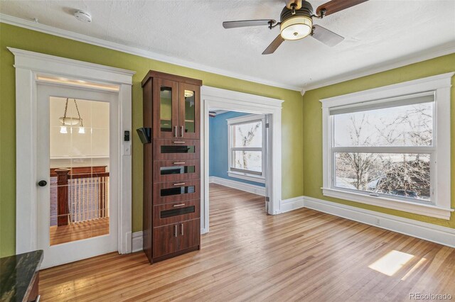 interior space with crown molding, baseboards, ceiling fan, and light wood-type flooring