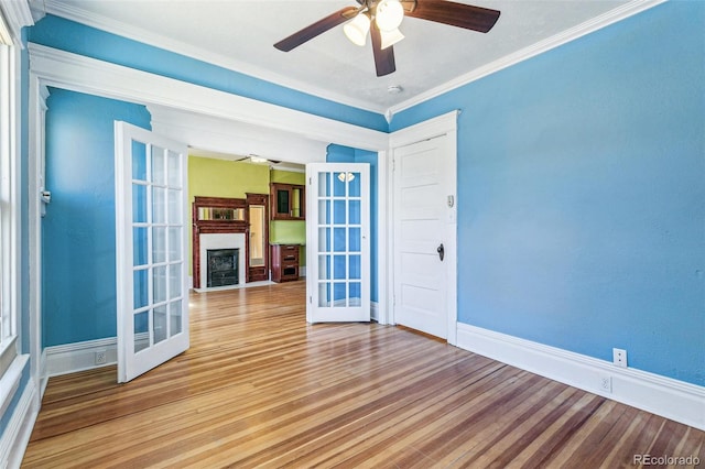 unfurnished room with a fireplace, ceiling fan, french doors, and wood finished floors