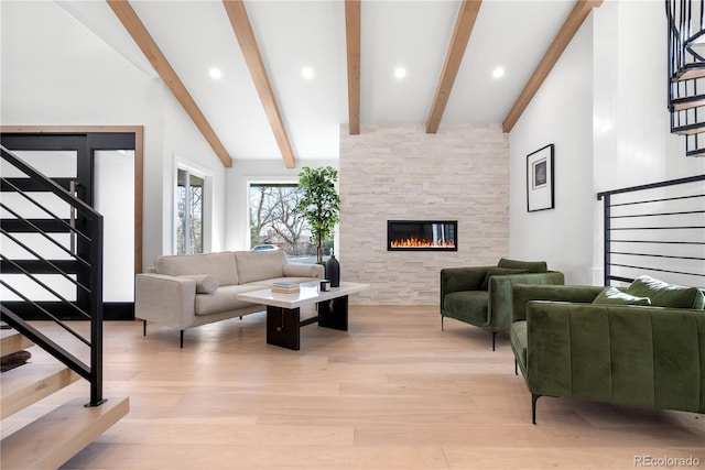 living room featuring vaulted ceiling with beams, light hardwood / wood-style flooring, and a stone fireplace