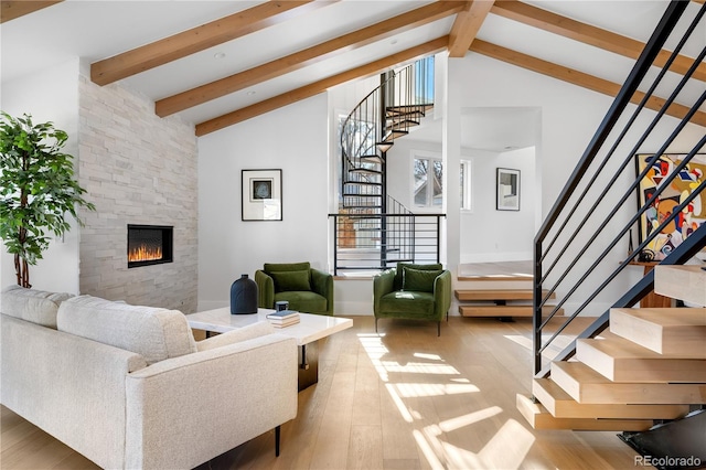 living room featuring vaulted ceiling with beams, light hardwood / wood-style floors, and a stone fireplace