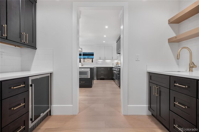 interior space featuring sink, wine cooler, decorative backsplash, light wood-type flooring, and appliances with stainless steel finishes